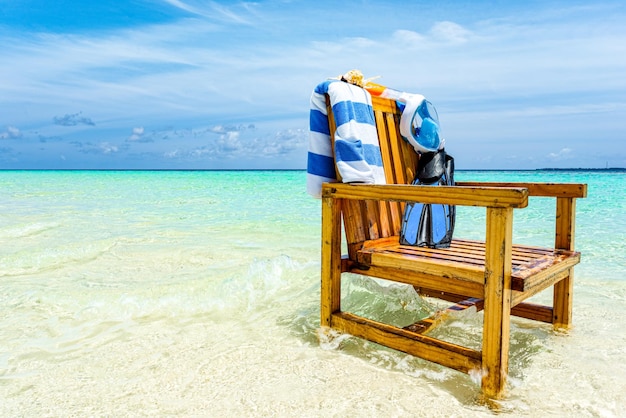 A wooden chair in the Indian Ocean with a towel shell flippers and inderwater mask