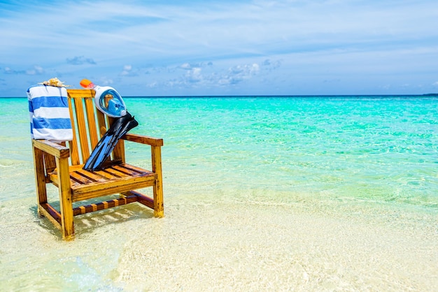 A wooden chair in the Indian Ocean with a towel shell flippers and inderwater mask