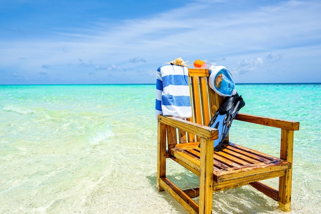 A wooden chair in the Indian Ocean with a towel shell flippers and inderwater mask