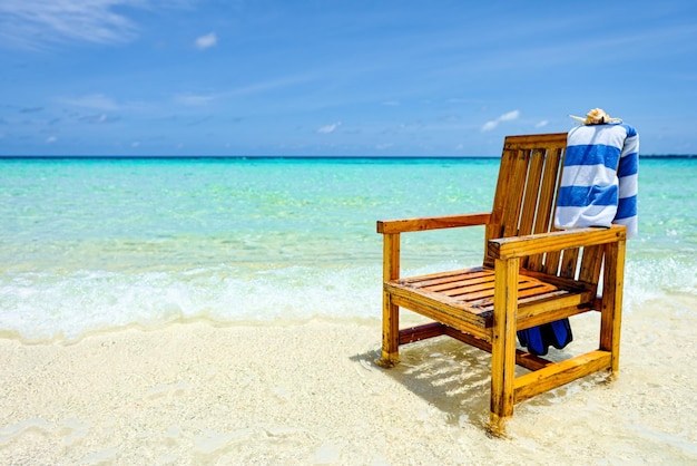 A wooden chair standing in the Indian Ocean with a towel shell and flippers