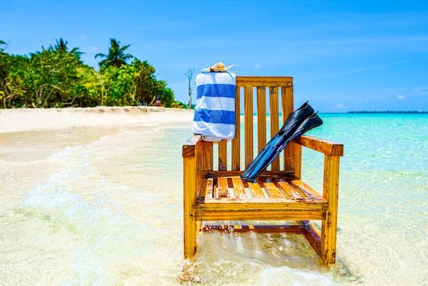 A wooden chair standing in the Indian Ocean with a towel shell and flippers