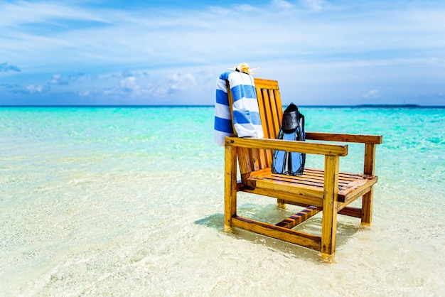 A wooden chair standing in the Indian Ocean with a towel shell and flippers