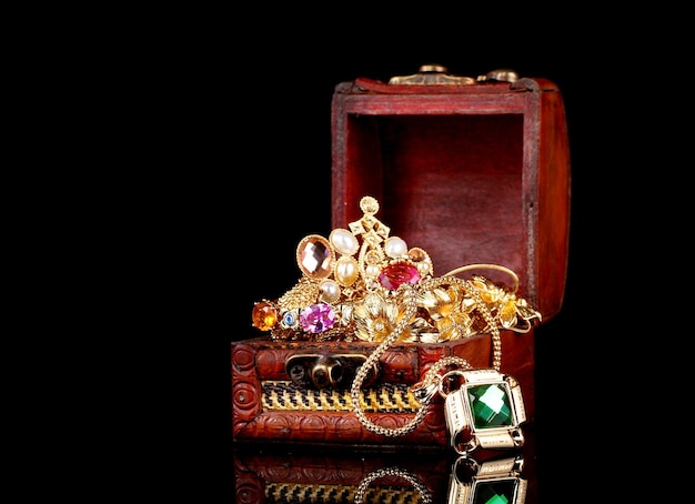 Wooden chest full of gold jewelry on black background