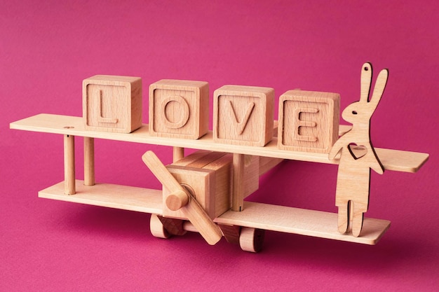 Wooden childrens plane and the word love made of cubes on a pink background Creative concept for Valentines day wedding trip romantic trip Bright postcard love background