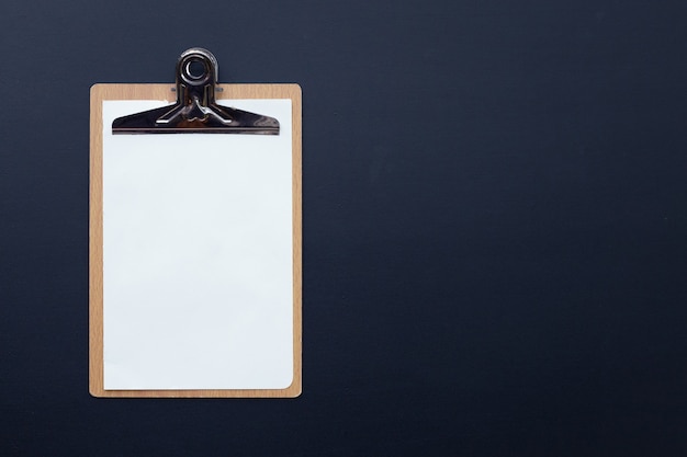 Wooden clipboard with blank white paper on dark background.