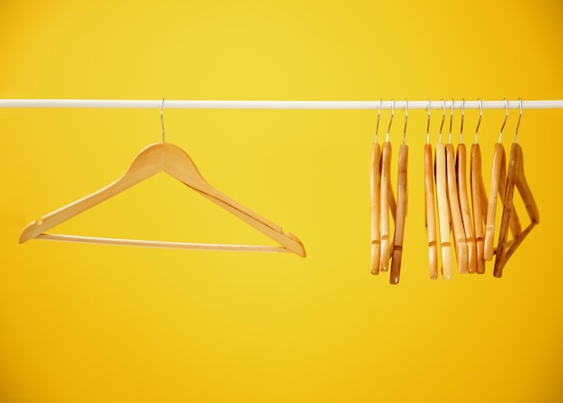 Photo wooden coat hangers on clothes rail and yellow background