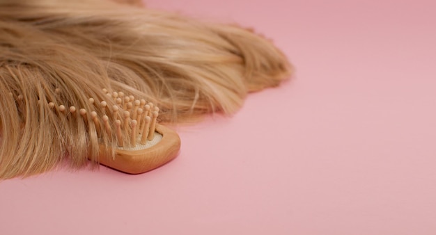 Wooden comb and blonde hair on a pink background with a place for text in the form of a banner