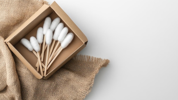 Photo wooden cotton swabs are neatly arranged in a kraft paper box resting on jute fabric illuminated by soft lighting that enhances the natural colors and fine details