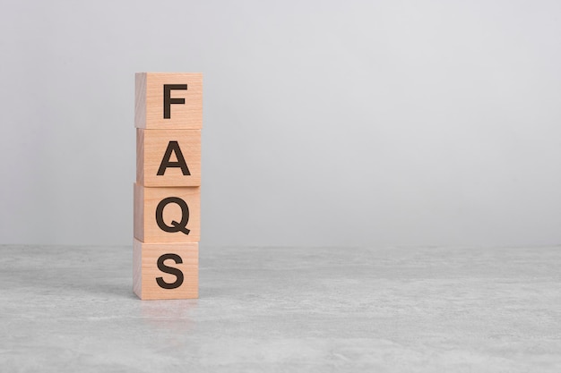 Wooden cube on a concrete surface with text FAQS copy space on right for design gray background