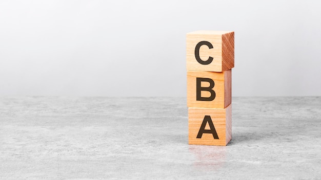 Wooden cube on a white table with text cba concept of business financial investment economy copy space on left for you design gray background CBA short for Cost Benefit Analysis