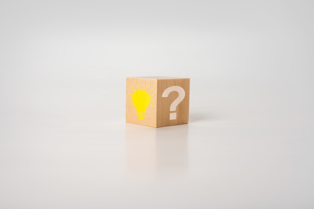 Wooden cube with bright light bulb and question mark on white table. Creative idea, Innovation and Solution concepts. Wooden cube with light bulb icon and question mark symbol.