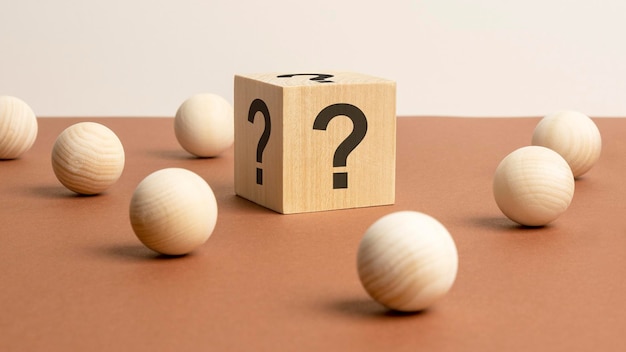 Wooden cube with a question mark surrounded by wooden balls on a brown table background