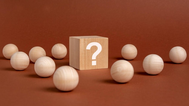 Wooden cube with a white question mark surrounded by wooden balls on a brown table background