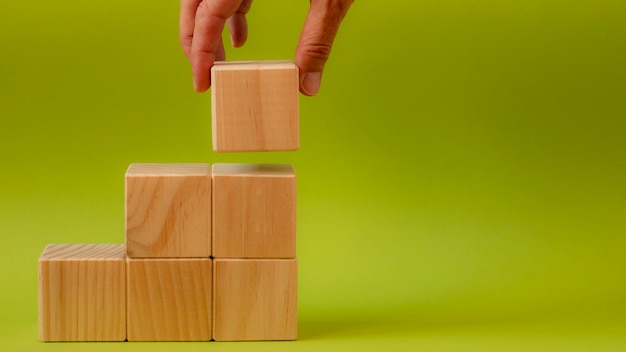 Wooden cubes stacked in the form of a podium on a pistachio green background and a person39s hand holding one of them