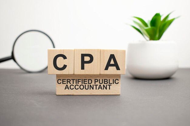 Wooden cubes with letters CPA Certified Public Accountant on white table with keyboard and glasses