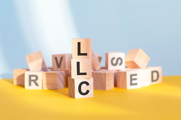 Wooden cubes with letters LLC arranged in a vertical pyramid, yellow background