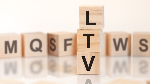 Wooden cubes with letters LTV arranged in a vertical pyramid, on the light background, reflection surface, business concept. LTV short for lifetime value