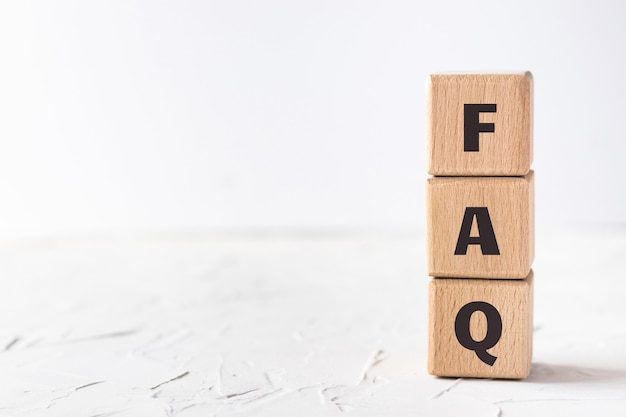 Wooden cubes with text FAQ on white putty texture background. Frequently asked questions. Flat lay, top view.