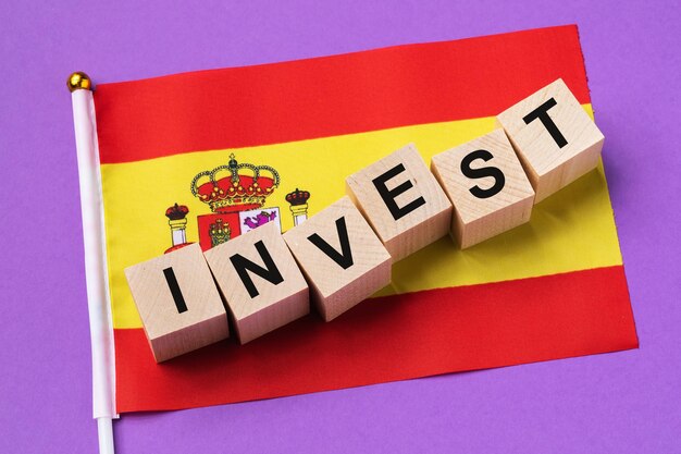 Wooden cubes with text and a flag on colored background concept on the theme of investment in Spain