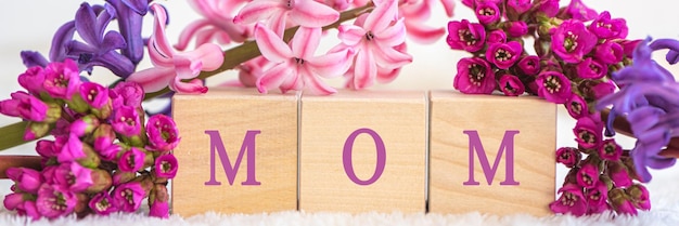 Wooden cubes with word mom and fresh flowers on white background