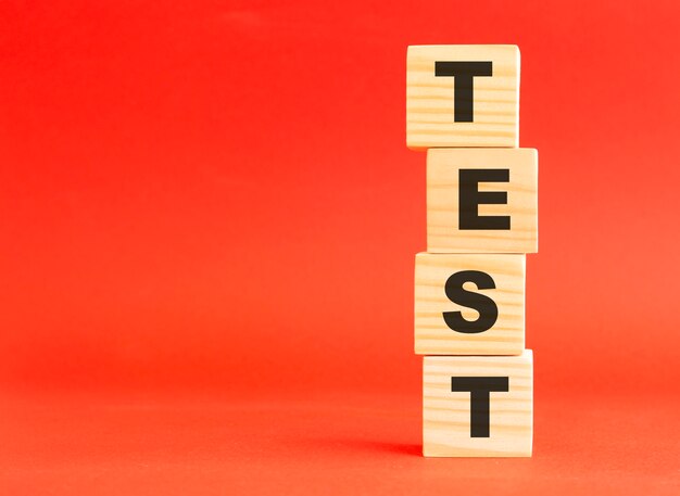 Wooden cubes with word TEST. For your design and concept. Wooden cubes on a red surface. Free space on the left.