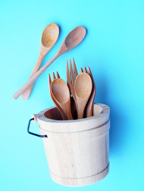 Above of wooden cutlery in bucket wooden spoon isolated on blue background