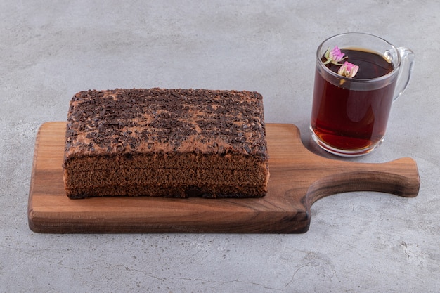 A wooden cutting board of chocolate cake and a cup of tea.