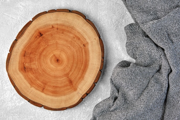 Wooden cutting board or dish coaster and gray kitchen towel on a light gray concrete table