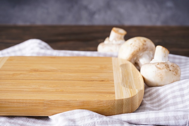 Wooden cutting board and mushrooms on a wooden background, place for text.