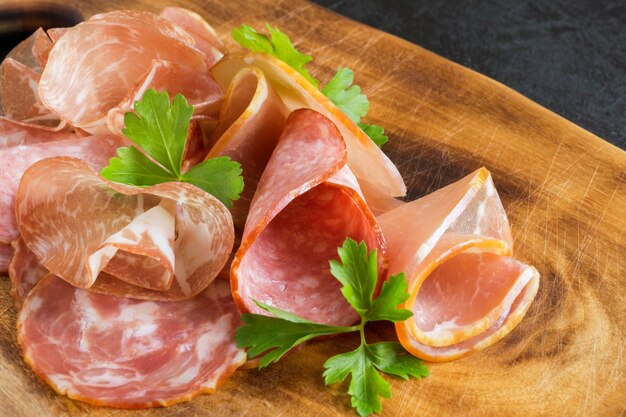 Wooden cutting Board with prosciutto, bacon, salami and sausages on a wooden background. meat platter