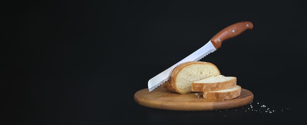 Wooden cutting board with sliced white bread and knife on black background