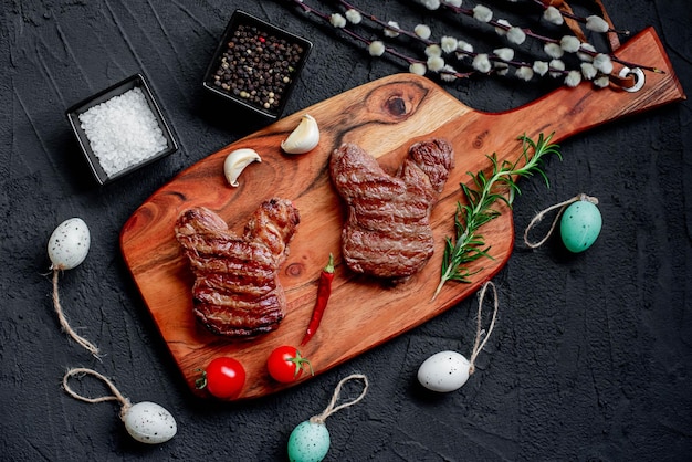 A wooden cutting board with steaks and eggs on a black background