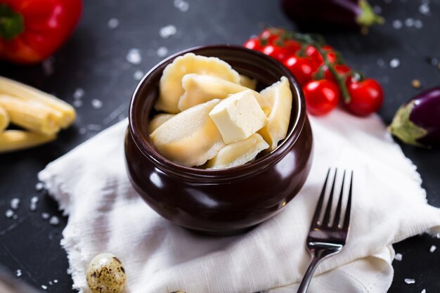 Photo on a wooden cutting kitchen board, dumplings with herbs in a clay pot, cherry tomatoes, cutlery on