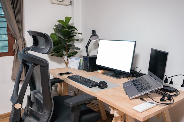 Wooden desk setting with laptop, display, mouse, lamp, ergonomic chair and artificial tree in workplace on bedroom