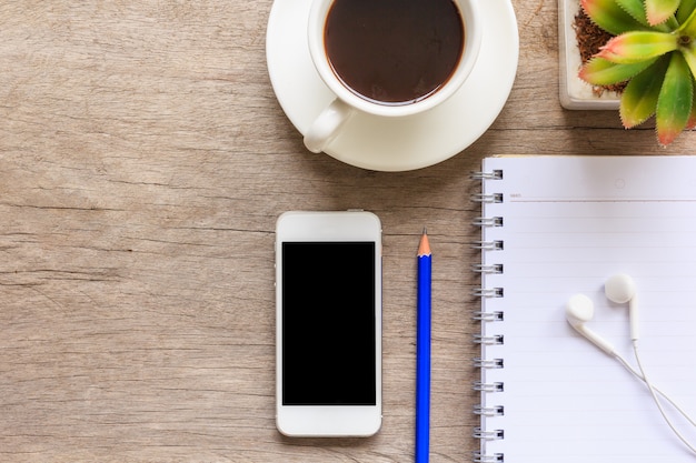 wooden desktop with notebook, earphones, smartphone, coffee cup, decorative plant 