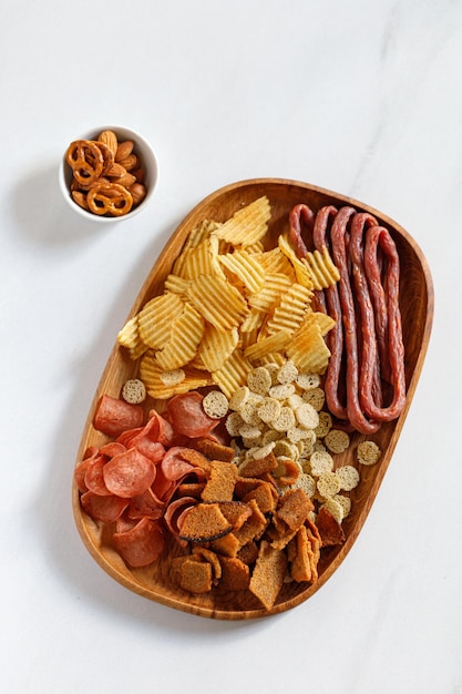 Wooden dish plate with beer snacks potatoes chips meat chips sausages kabanos White background