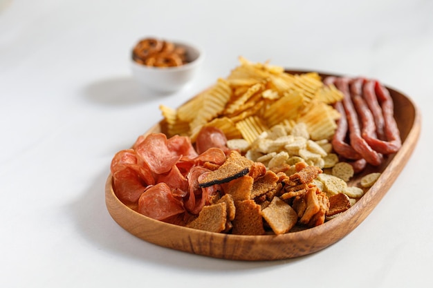 Wooden dish plate with beer snacks potatoes chips meat chips sausages kabanos White background