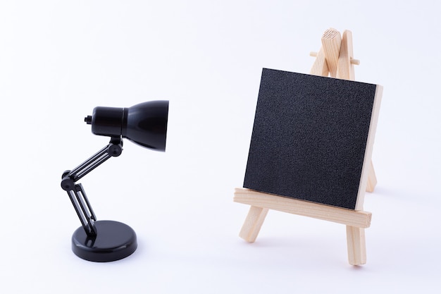 Photo wooden easel miniature with blank black square canvas and table lamp