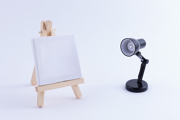 Photo wooden easel miniature with blank white square canvas and table lamp