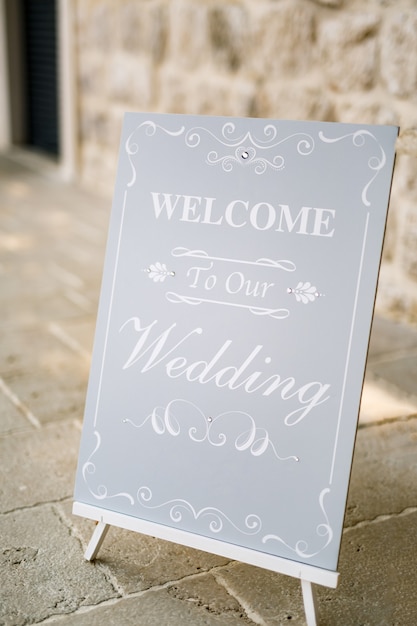 Wooden easel with inscriptions stands in front of an ancient building inscription welcome to our wedding