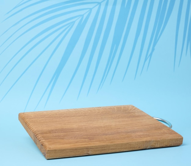 Wooden empty cutting board at an angle on a blue background kitchen utensils