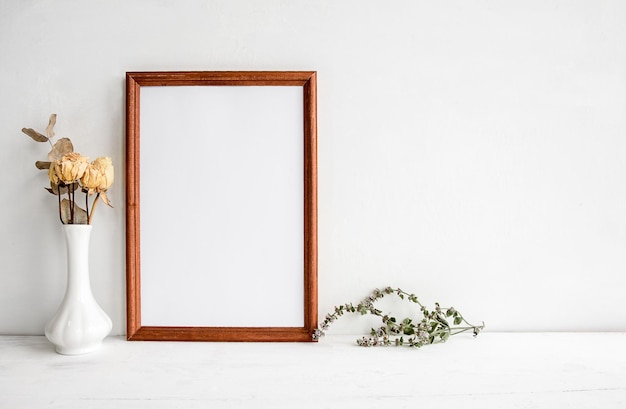 A wooden empty photo frame on a white table and flowers in a vase A fashionable wedding or holiday banner