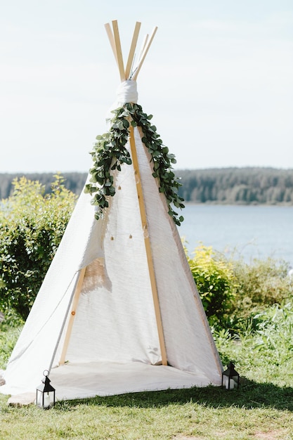 Photo wooden fabric wigwam decorated with green eucalyptus branches in the backyard event or wedding