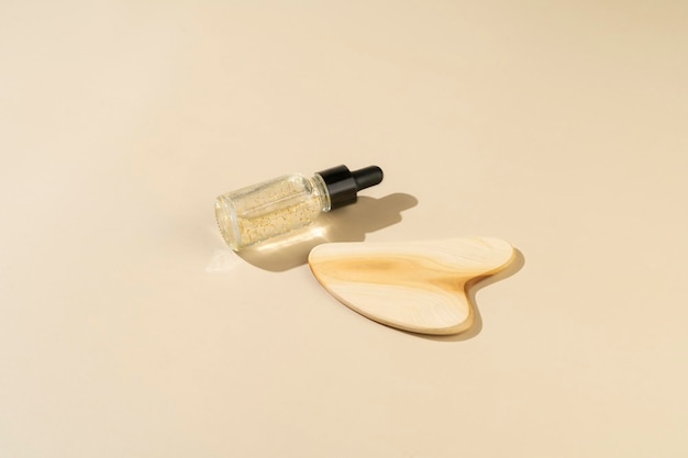 A wooden face massager and an antiaging serum with golden parts lying on a beige background