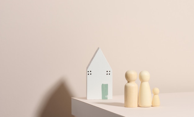 Wooden family figurines, model house on a beige background. Real estate purchase, rental concept. Moving to new apartments