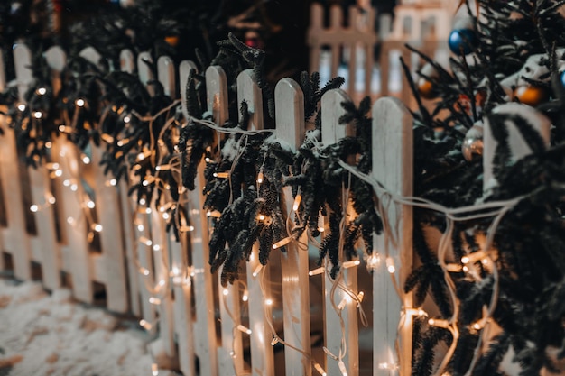 Wooden fence decorated with golden garlands and New Year's branches in the snow