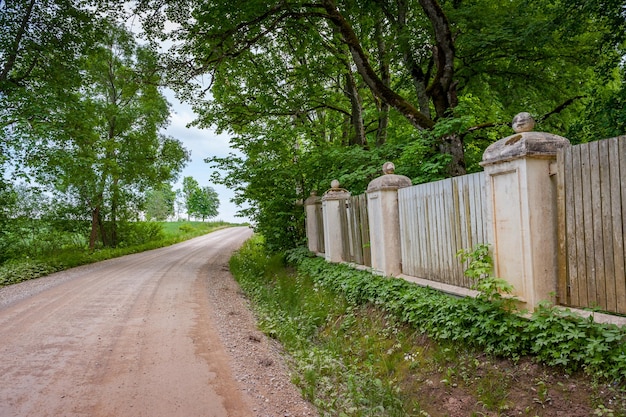 Wooden fence with stone columns and  floor Tree and fence along a dirt road