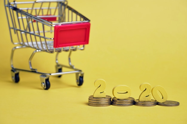 Wooden figures 2020 on stacks of coins near a trolley background