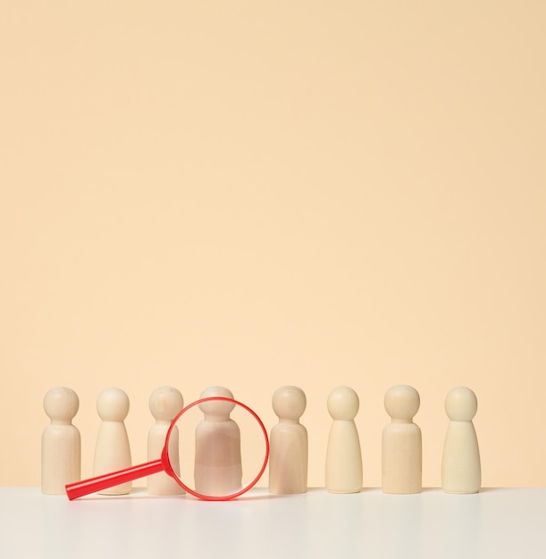 Wooden figures of men stand on a beige background and a blue plastic magnifying glass