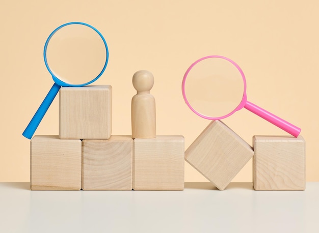 Wooden figures of men stand on a beige background and a blue plastic magnifying glass